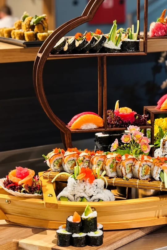 Dřevěná sushi loď s rolkami, nigiri a květy