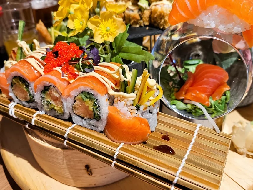 Sushi rolky s lososem, nigiri a jedlé květy na dřevěném podnose